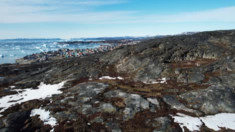 Small-township-behind-rocky-hill-in-Greenland,-aerial-drone-view