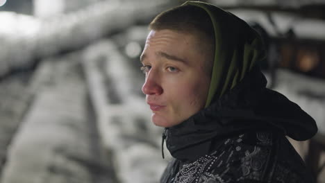 side profile of street boy in hoodie looking around under night light near snowy seating area, with cold air visible on face and soft lighting casting reflective tones over winter surroundings