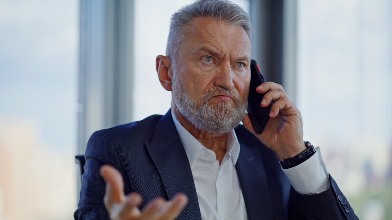 Primo piano di un direttore infastidito che parla al cellulare seduto in ufficio. Manager senior