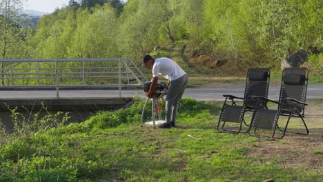 Man-setting-up-bbq-dinner-at-campground-in-Norway,-afternoon-sunshine