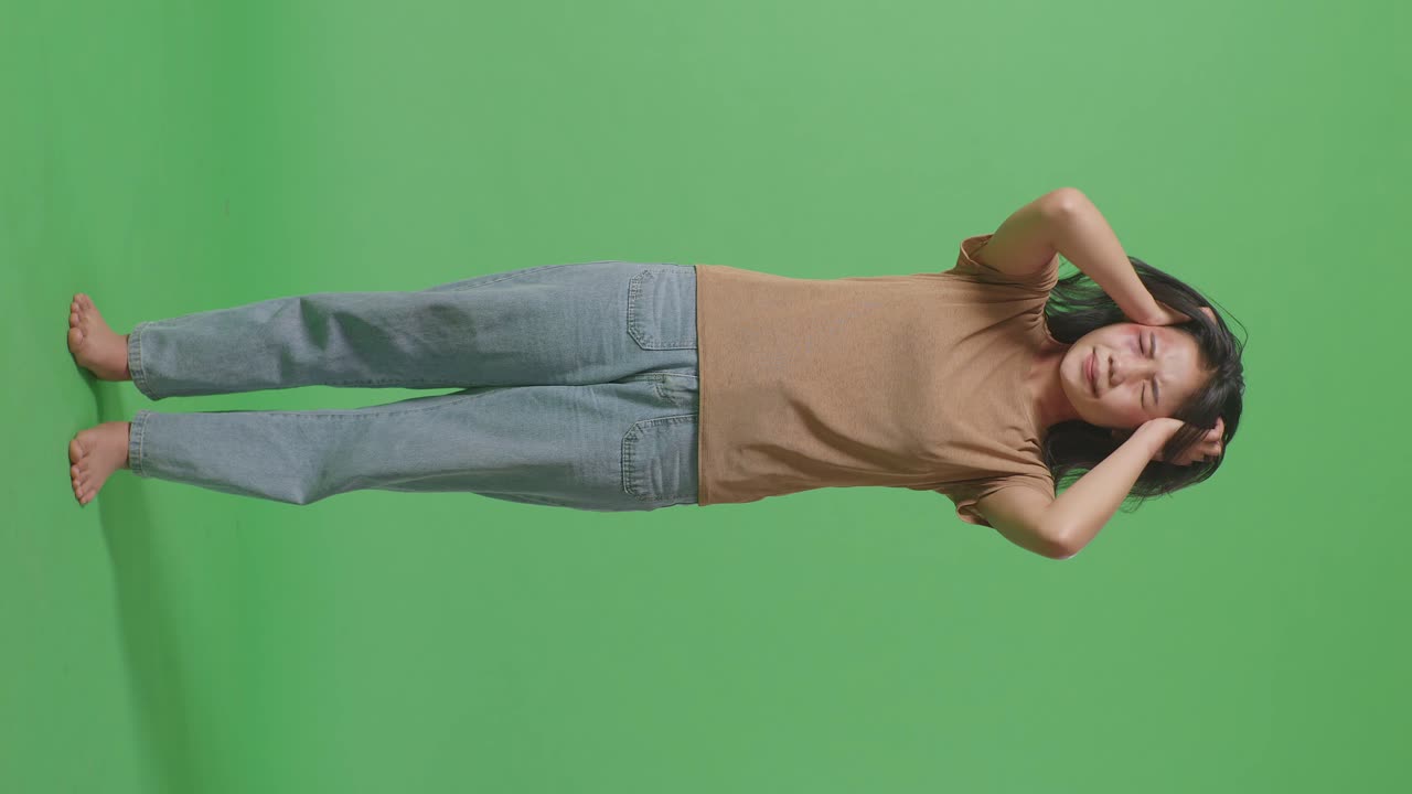 젊은 아시아 여성이 폭력의 희생자로 몸에 이 있고 신경 붕괴를 겪고 녹색 스크린 배경 스튜디오에서 비명을 지르고 있습니다.