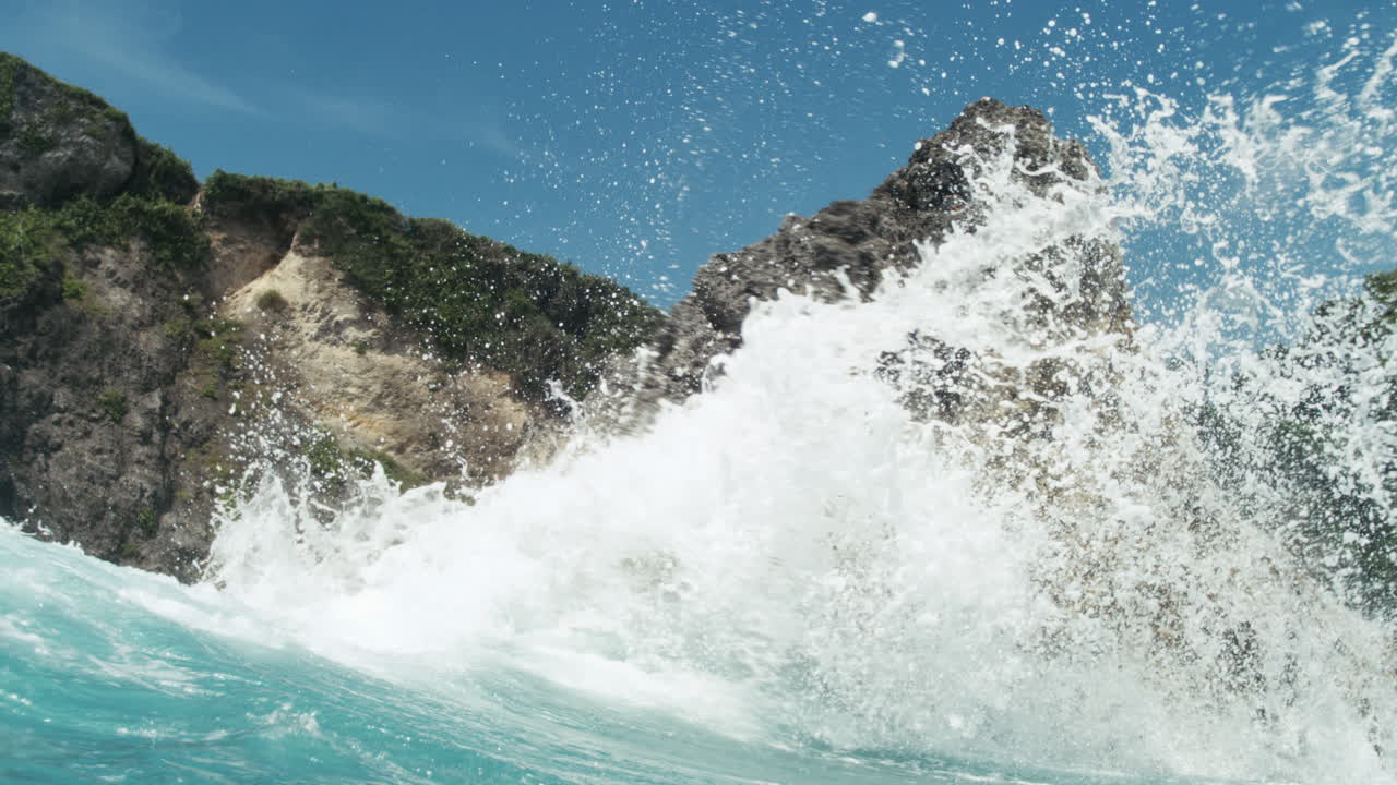 Surging turquoise waves smash against jagged volcanic rocks, slow motion slowmo backdrop