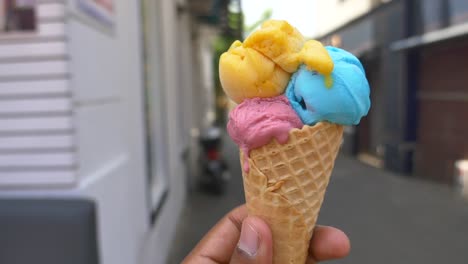 handheld colorful ice cream cone in city street