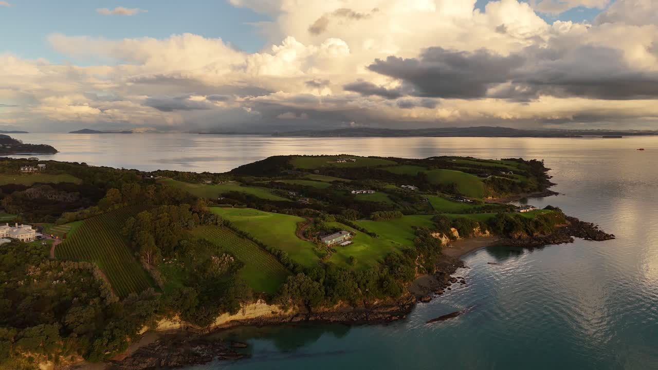 Waiheke Island, lush coastline, beautiful sunset sky and clouds reflecting in calm ocean water, New Zealand. Aerial drone