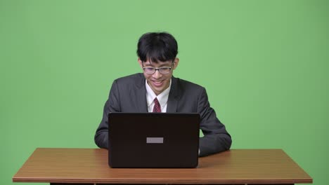 젊은 행복 한 아시아 사업가 가 노트북 을 사용 하면서 미소 짓고 있다