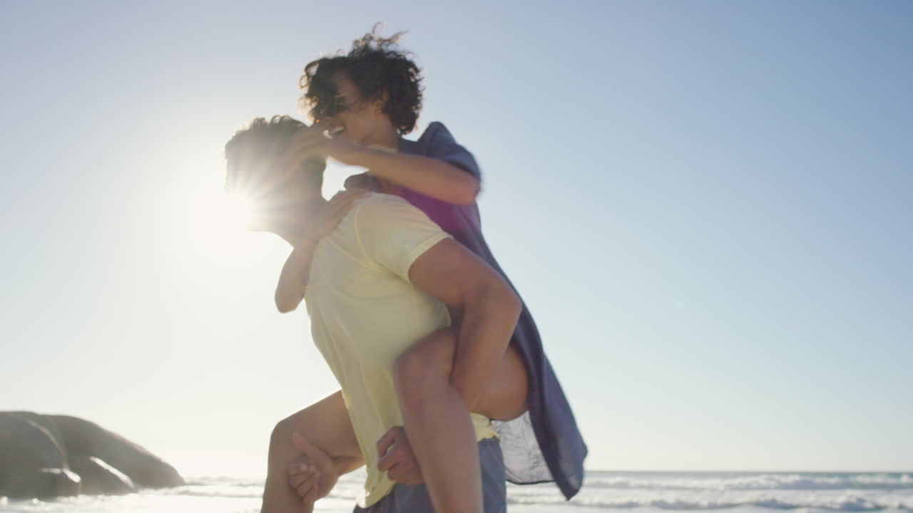 hombre atractivo dando novia piggyback pareja de raza mixta disfrutando de la naturaleza en la playa