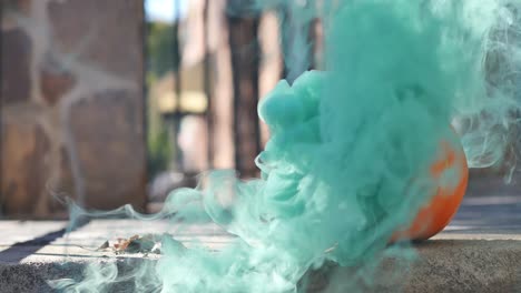 Green-smoke-wafting-out-of-orange-jack-o-lantern-sitting-on-urban-porch