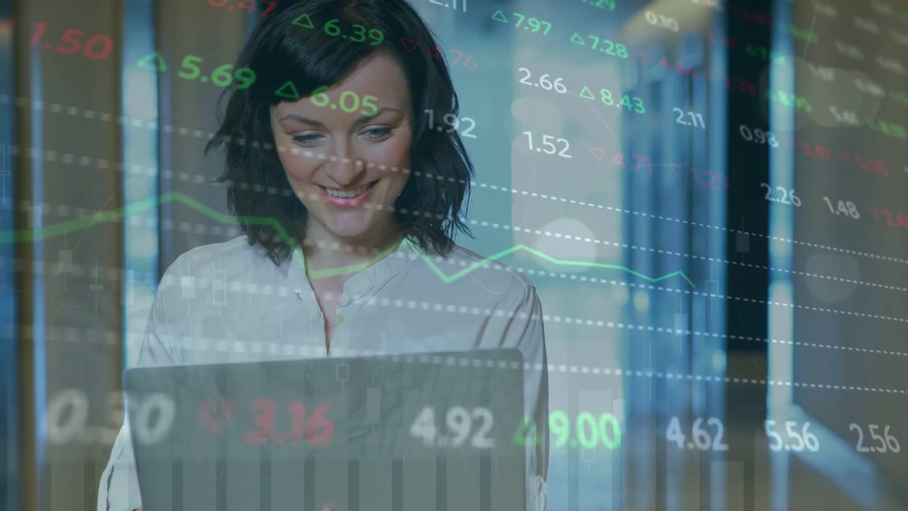 Mujer leyendo en un portátil en una oficina, monitoreando indicadores financieros superpuestos en el marco y sonriendo ante las ganancias.