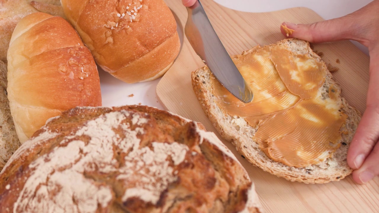 Primo piano di burro d'arachidi spalmato sul pane tra pane a lievitazione naturale, baguette e croissant.