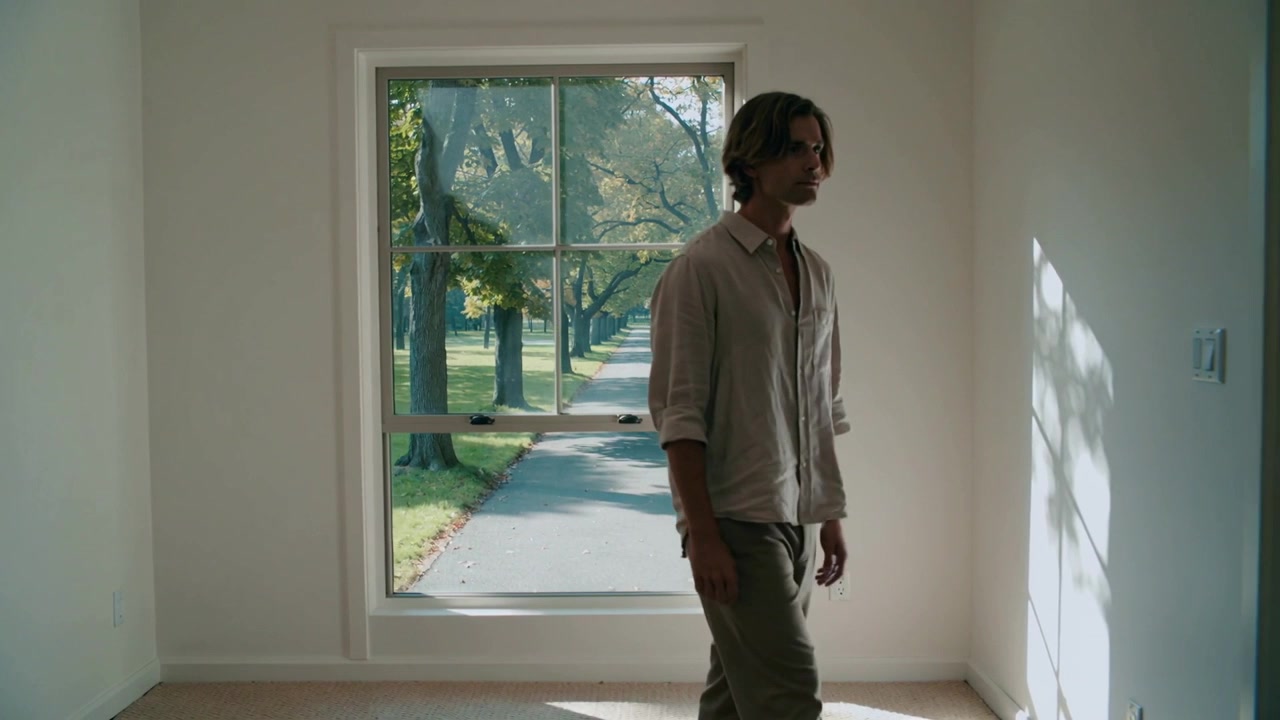 Shifting weight, man walking slowly past window, in rolled sleeves shirt, checking sunlit wall