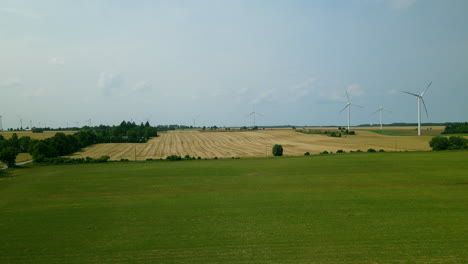 Schöne-Ländliche-Landschaft-Mit-Blick-Auf-Ein-Gemähtes-Feld-Mit-Maisstoppeln-Und-Windmühlen,-Die-Sich-Im-Wind-Drehen,-Ernten-Schuss-Für-Luftschuss,-Polen