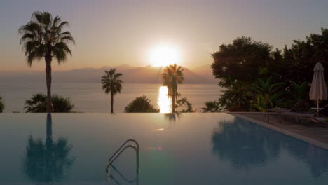 vacation scene with swimming pool overlooking sea and mountains at sunset