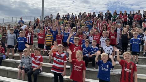 a large gathering of children in colorful jerseys celebrating together at a stadium, creating a joyful atmosphere of camaraderie and team spirit