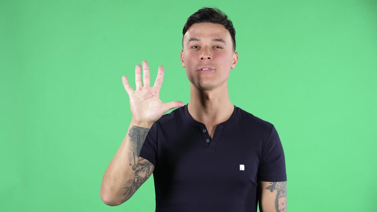 retrato de un joven guapo está mirando los espectáculos de la cámara y contando uno, dos, tres, cuatro, cinco dedos. pantalla verde