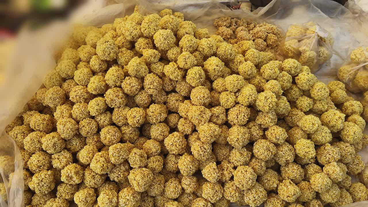 Ripresa in movimento su murmura ladoo appena preparati, fatti con riso soffiato e jaggery, che mostra dolcetti rotondi uniformi, una consistenza ricca e la preparazione di uno spuntino tradizionale indiano.