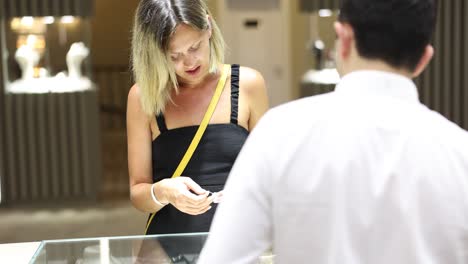 a woman shopping for jewelry at a store, assisted by a salesperson