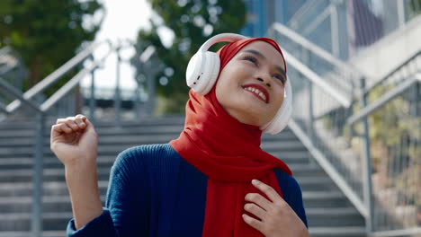 joyful young woman in hijab listening to music with headphones outdoors