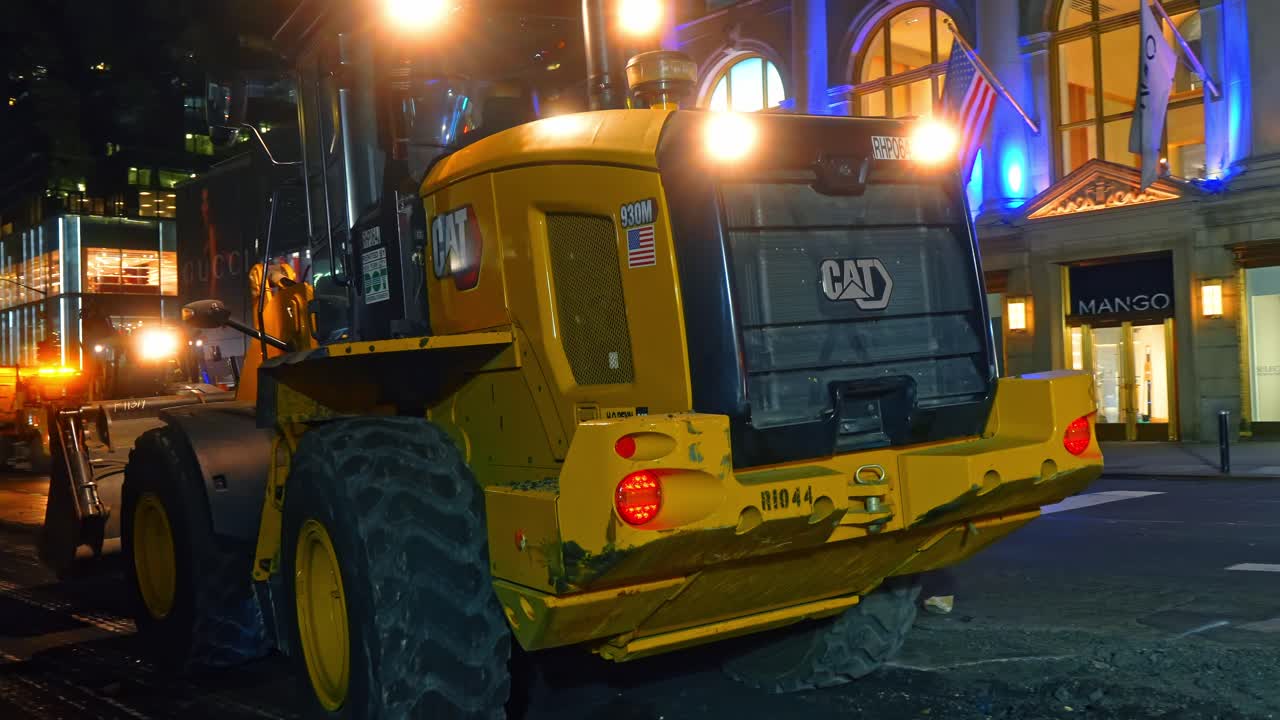 New York, USA, 5 October 2025: Close up of CAT front loader during night construction. Front view of a Caterpillar wheel loader with headlights on during nighttime street repairs in New York City