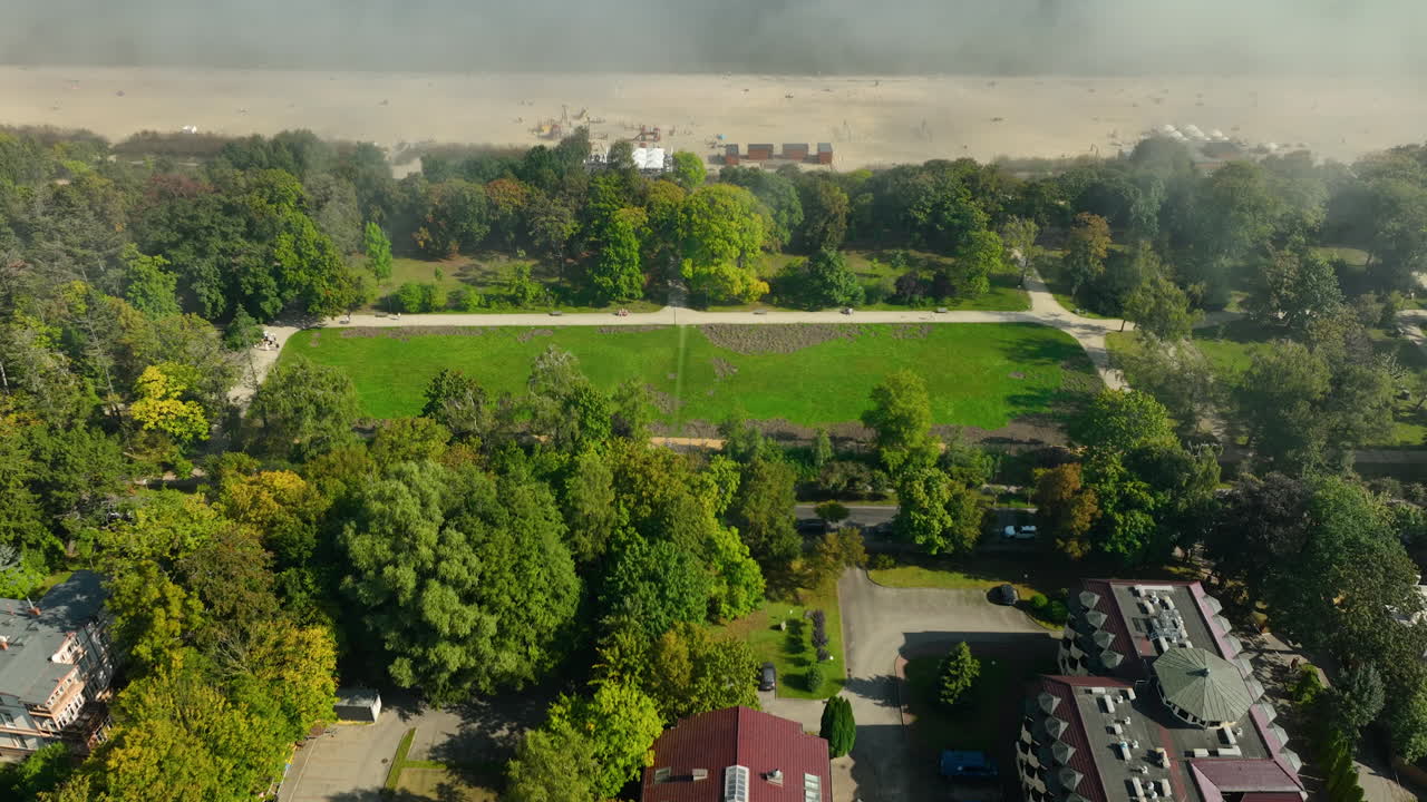 An aerial shot showing Sopot’s green parkland merging into fog, with sandy beaches and the sea hidden under a thick mist.