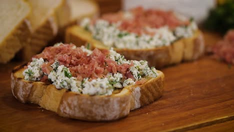 Tasty homemade bruschetta with ham on white cheese served in a wooden cutting board - macro, close up slider movement