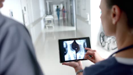 diverse doctors talking and using tablet in hospital corridor, slow motion