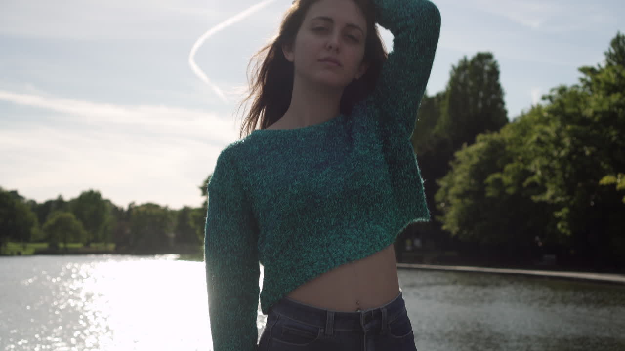 cámara inclinándose hacia arriba revelando una hermosa modelo de moda italiana posando con su atuendo en un parque en londres a la hora dorada