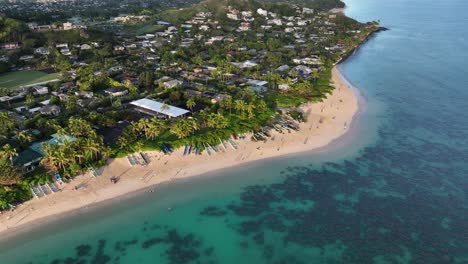 Schwenkende-Drohnenaufnahme-Des-Strandes-Von-Lanikai-Bei-Sonnenaufgang-Mit-Klaren-Riffen,-Palmen,-Immobilien-Am-Meer,-Kanus-Und-Strandgängern-Auf-Oahu,-Hawaii