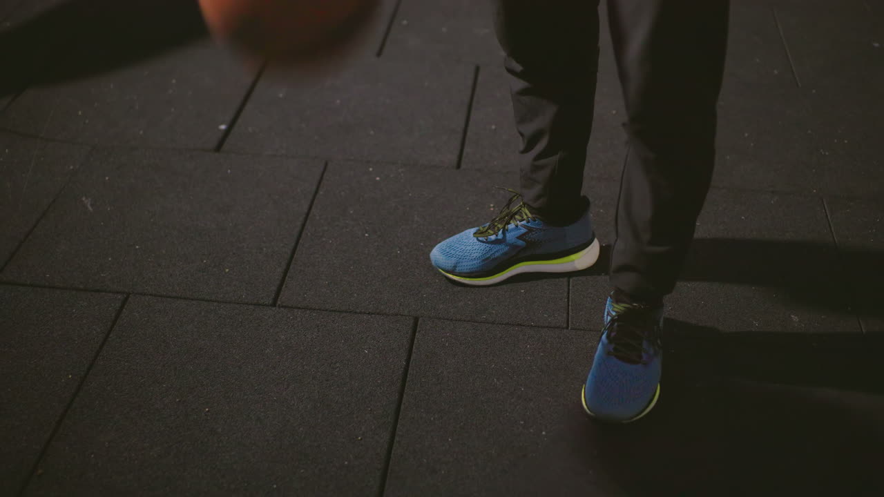 primer plano nocturno de zapatillas azules realizando movimientos lentos y sutiles en una cancha urbana de goma, un atleta solitario practicando el equilibrio y la agilidad, sombras profundas y asfalto texturizado que crean un ambiente tranquilo