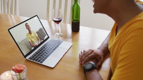 Mid-section-of-african-american-man-talking-on-video-call-on-laptop-at-home