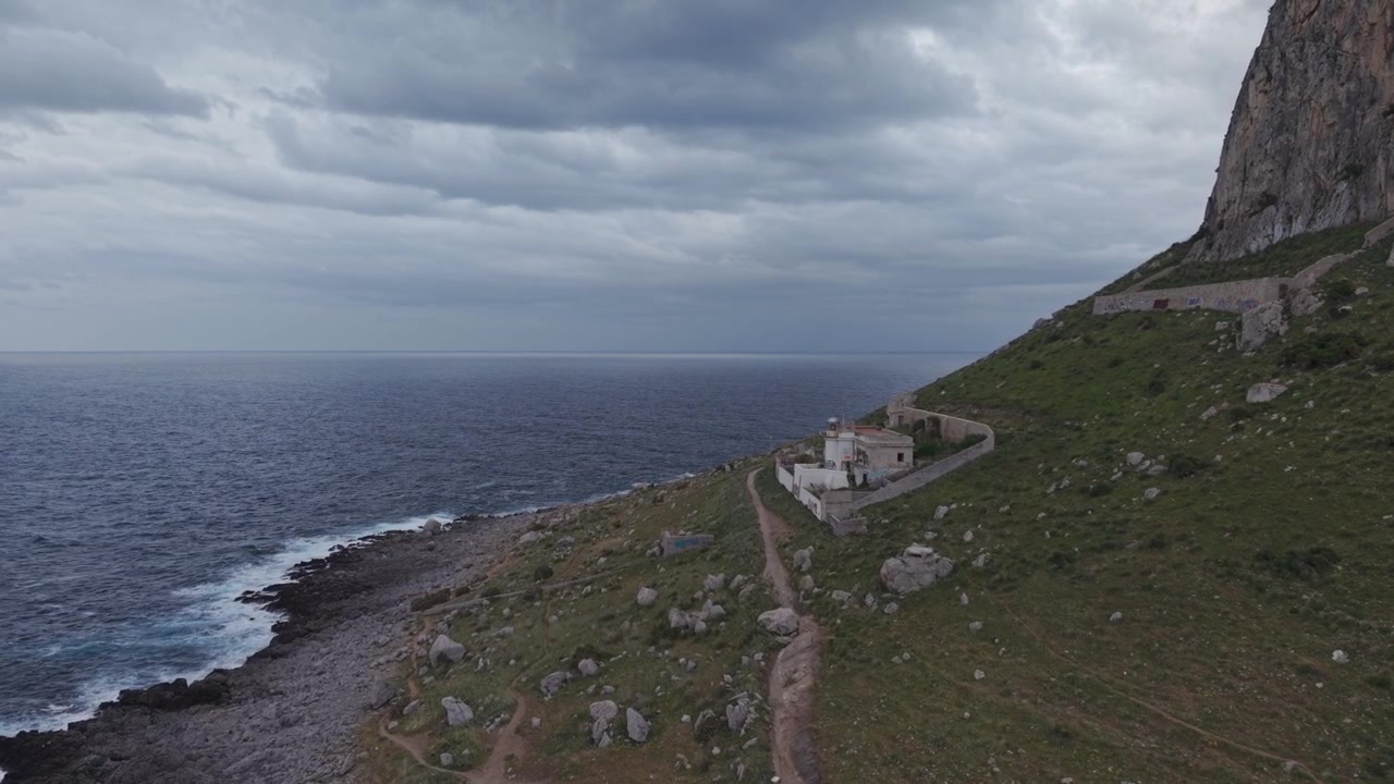 Costa rocciosa e paesaggio oceanico sotto un cielo nuvoloso e drammatico con un faro.