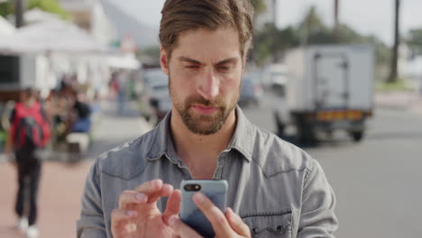 Retrato-De-Un-Joven-Atractivo-Usando-Un-Teléfono-Inteligente-Enviando-Mensajes-De-Texto-Navegando-Disfrutando-De-La-Satisfacción-De-La-Comunicación-Móvil-Revisando-Mensajes-En-Cámara-Lenta-Frente-A-La-Playa-Urbana-De-Sunner