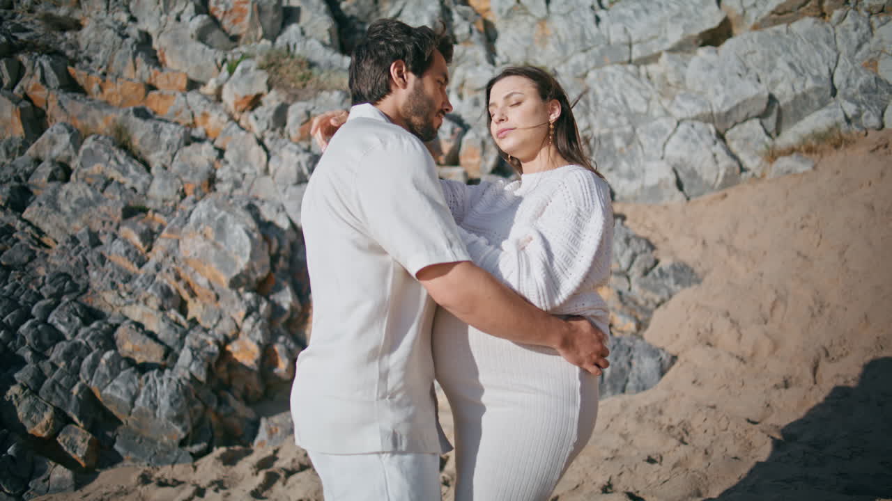una pareja embarazada disfruta del fin de semana en la naturaleza de pie en la orilla del mar. futuros padres abrazándose.