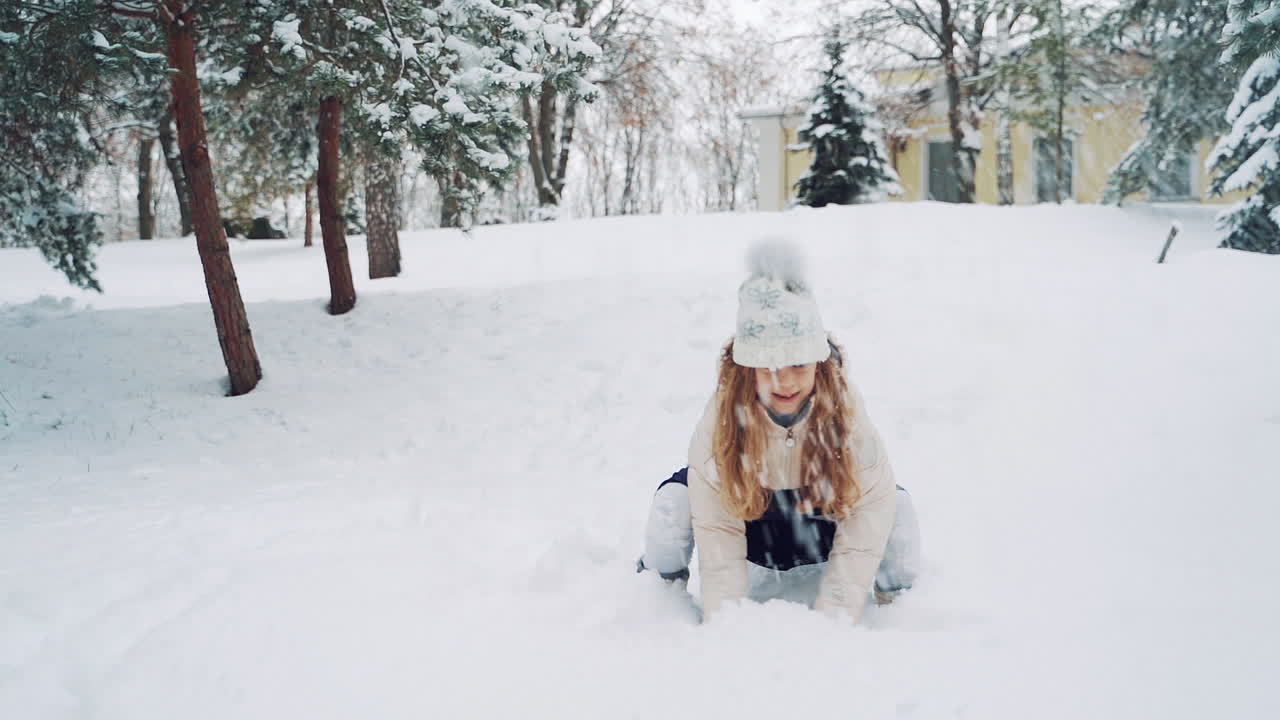 Pretty girl is playing with snow in the park in winter. Active kid throws up white snow and has a lot of fun with it outdoors. Slow motion.