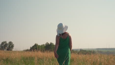 joyful lady in green dress with white hat dancing freely in golden field near trees under warm sunlight, arms outstretched in delight, embracing freedom, nature, and peaceful outdoor adventure