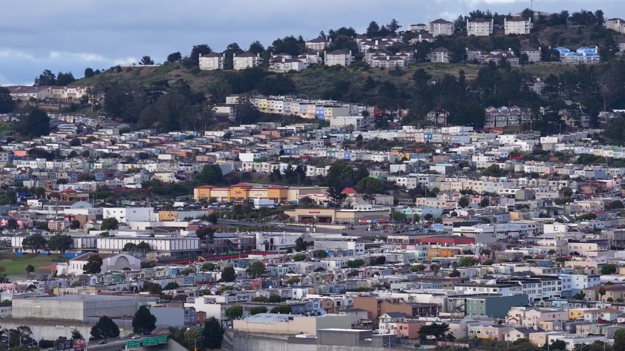 Veduta aerea di Daly City che rivela file di case residenziali situate lungo dolci colline, con nebbia costiera che si sposta tra le strade e i tetti in un tranquillo scenario della California settentrionale.