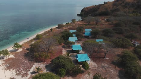 aerial drone shot of the island house's roofs surrounded of amazing turquoise ocean water with coral reefs and nature