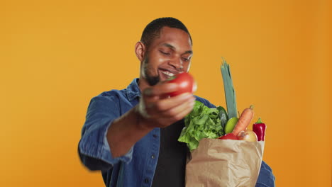 Young-vegan-guy-presenting-a-ripe-freshly-harvested-tomato-on-camera