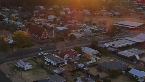 drone camera glides over suburban coonabarabran, australia at sunset, revealing rooftops, tree-lined streets, and warm golden hour lighting