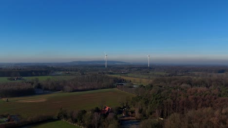 aerial establishing shot of forest landscape of america with forest in winter season. sunny day with blue sky and rotating wind turbines. wide shot. colored scenery in american countryside.