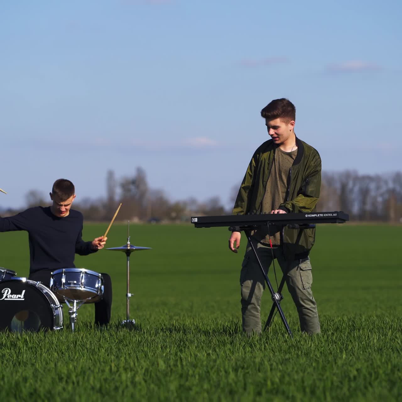 Musicians performing music playing the drums and piano. Members of boys' band play music and dance in the field. Highway with cars at the backdrop
