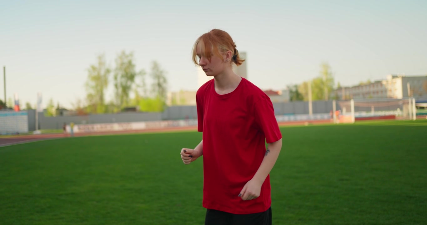 Young Woman in Red T-shirt Walking on a Green Stadium Field