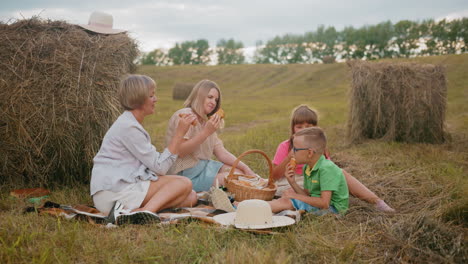 happy family seated on grass enjoying fresh pastries from picnic basket, young boy in green shirt eats immediately while girl in pink shirt carefully picks her choice as they share a meal outdoors