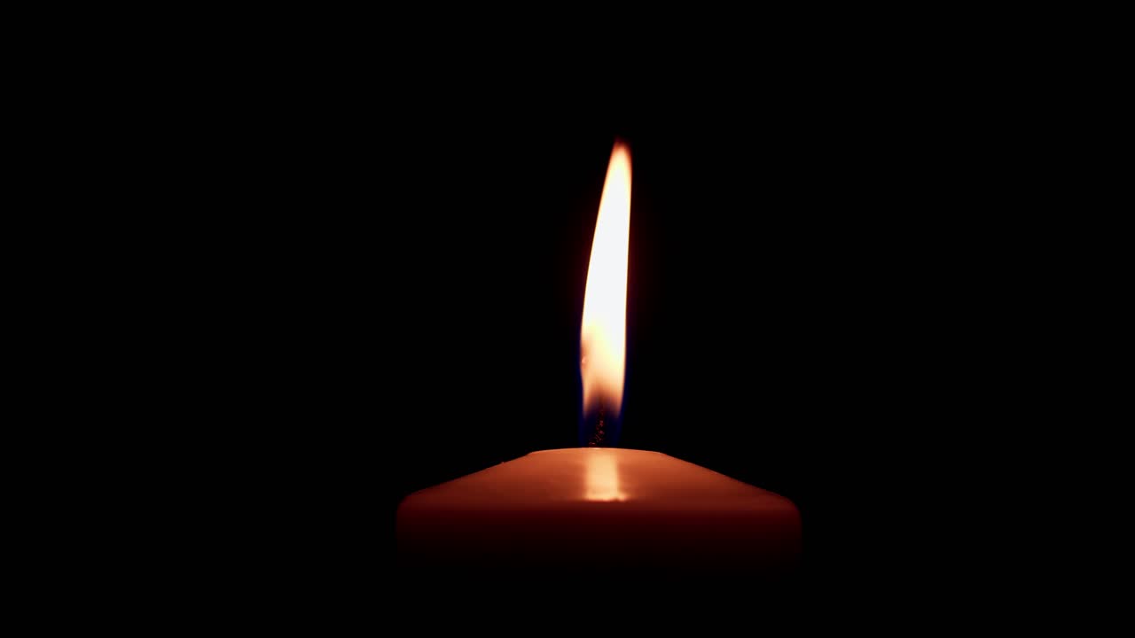 una sola llama de vela amarilla grande se enciende y se apaga, aislada en un fondo negro