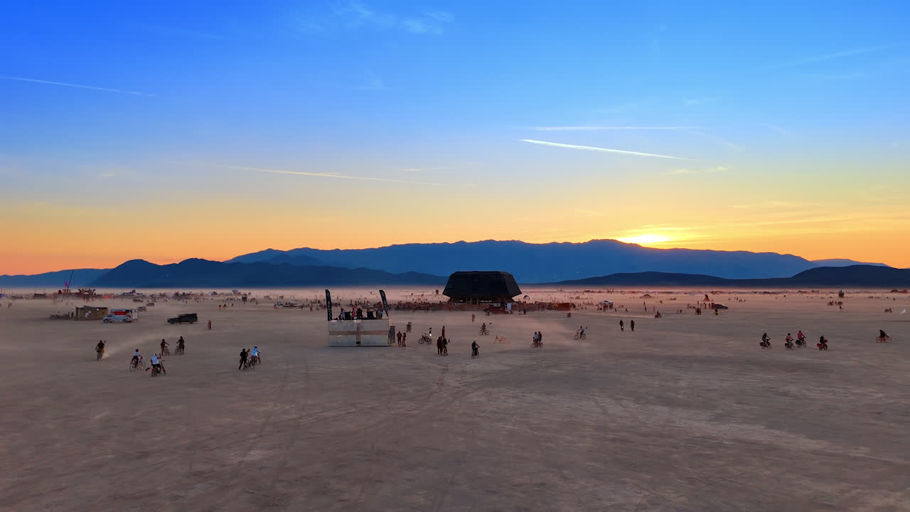 Nevada, USA, 14 August 2025: Burning Man playa view with festival crowd and sunset in Nevada desert.. Participants spread across the playa with mountains on the horizon