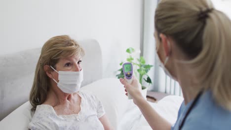 Female-health-worker-checking-temperature-of-senior-woman-at-home