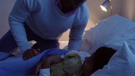 Father-giving-goodnight-kiss-to-his-son-while-sleeping-on-bed