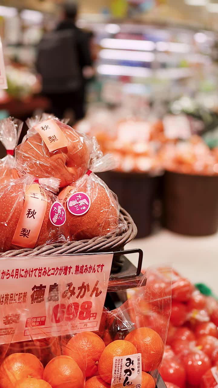 日本の食料品店の陳列棚に並べられた、パッケージされた梨とオレンジのクローズアップ