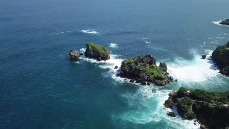 Aerial-view-showing-blue-colored-ocean-waves-crashing-against-coral-rocks-at-Timang-Island,Indonesia