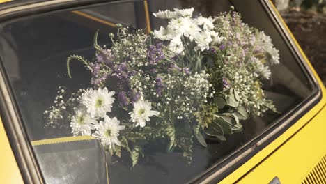 bouquet of white and purple flowers placed on the rear window of a yellow vintage car, creating a classic look