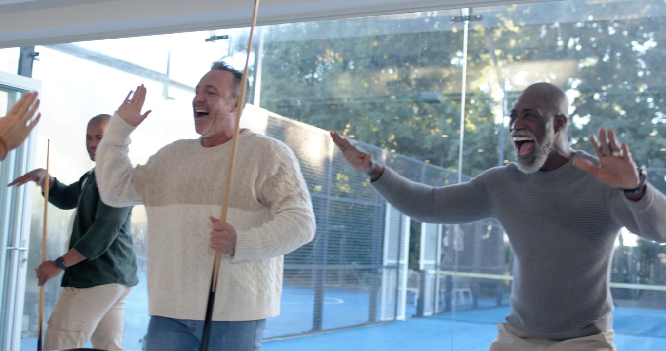 Four men around pool table in glass lounge shooter bracing, aiming, striking cue ball cheering